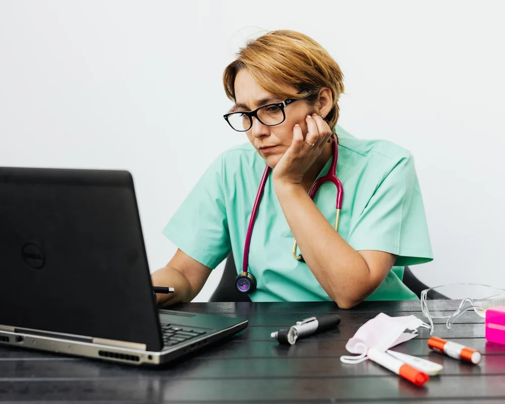 A clinician at her desk reviewing a note on her laptop.